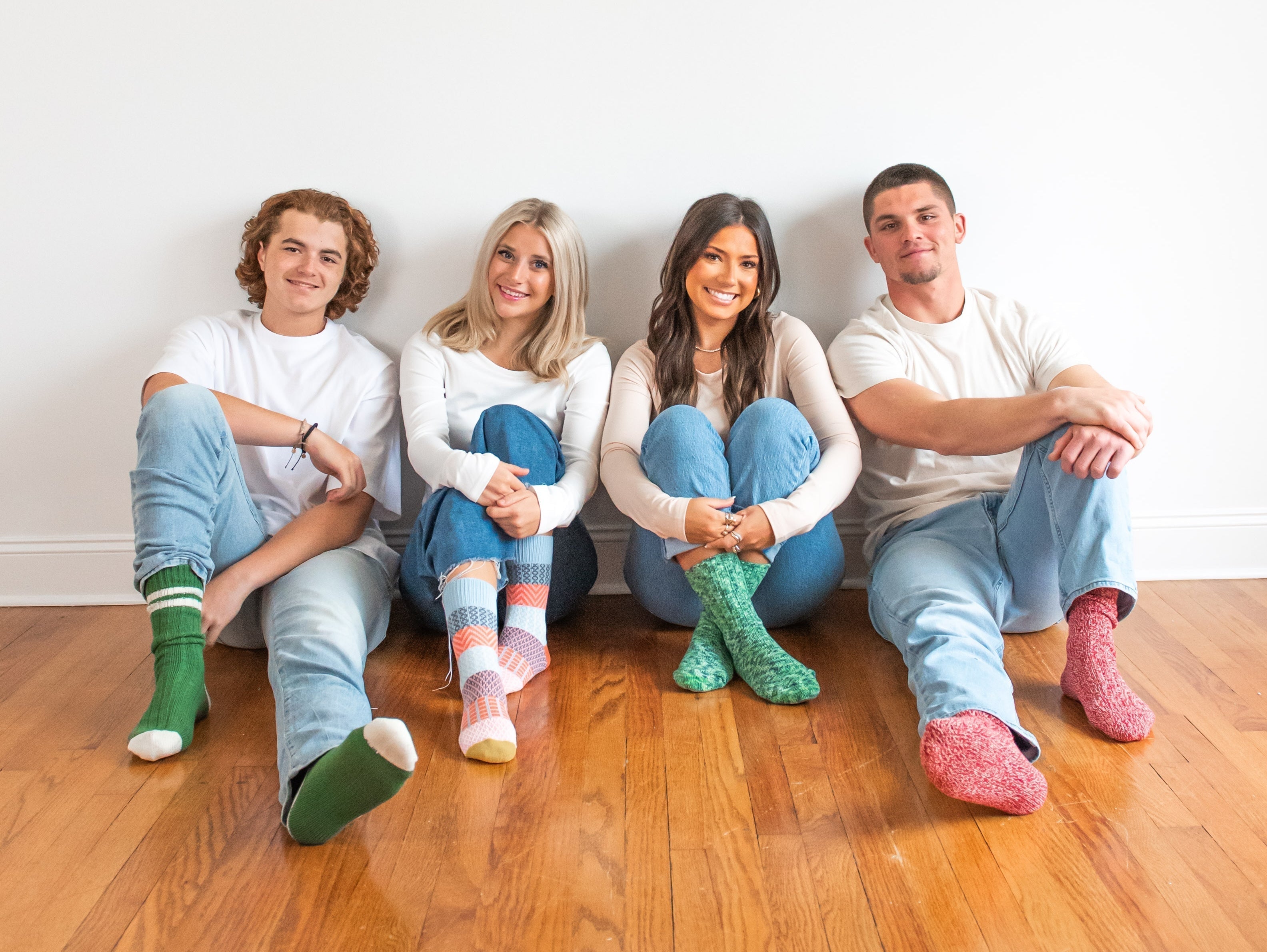 4 young adults sitting on wood floor in jeans, tshirts, and crew socks